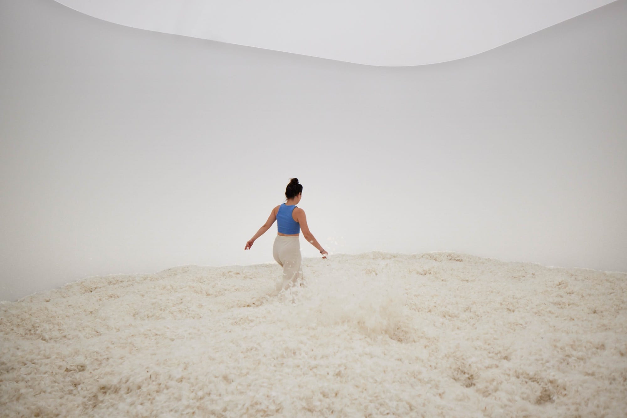 a white woman wades through a pile of white feathers