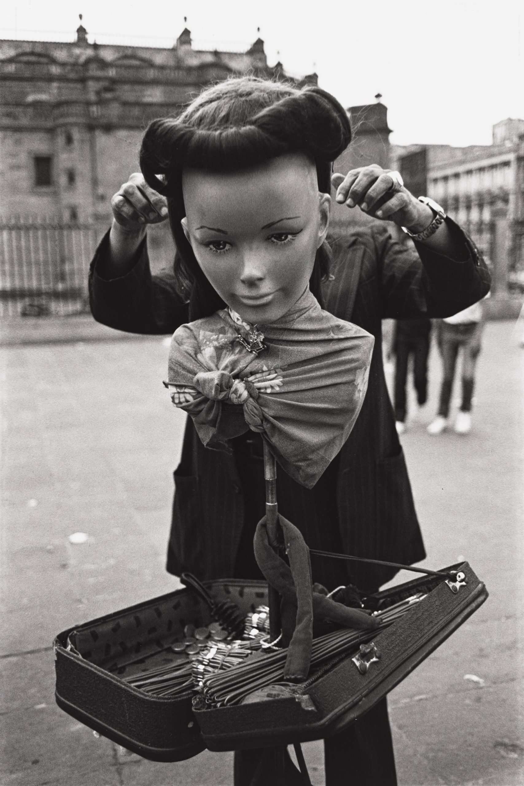 a black-and-white photo by Yolanda Andrade of a street performer with a large mask of a woman