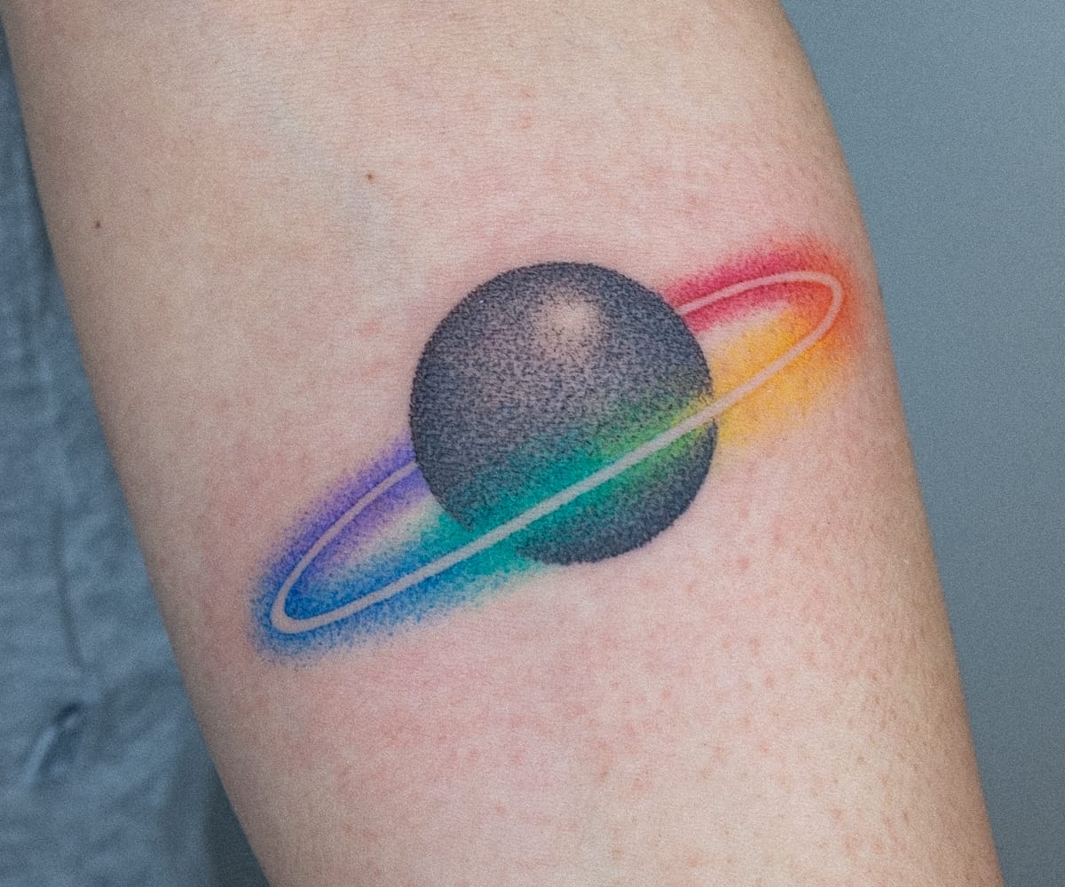 a white arm with a tattoo by Nano Ponto of a vibrant gradient circling a planet