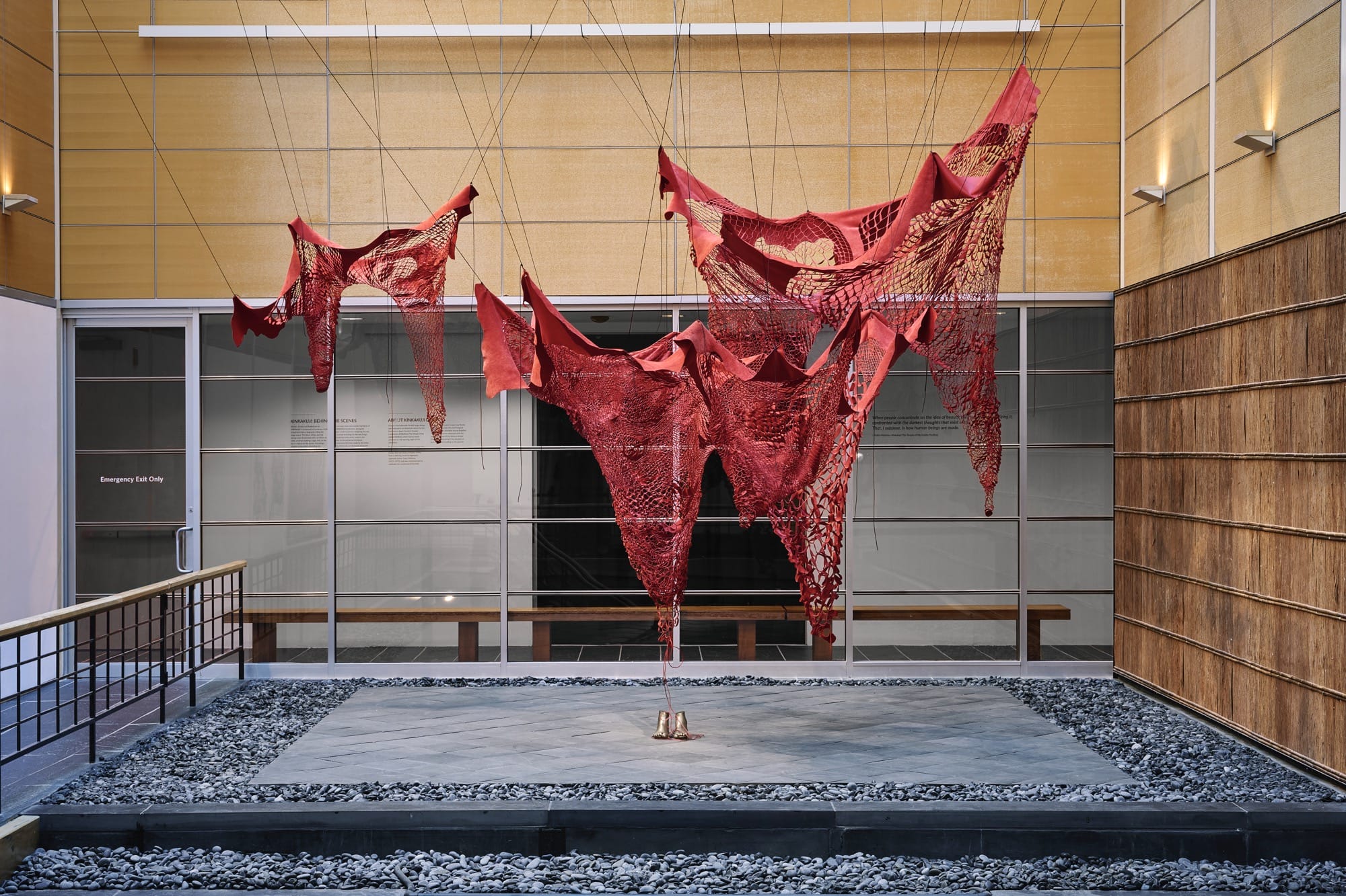 an outdoor installation by Chiharu Shiota of red fiber suspended above a pair of bronze shoes