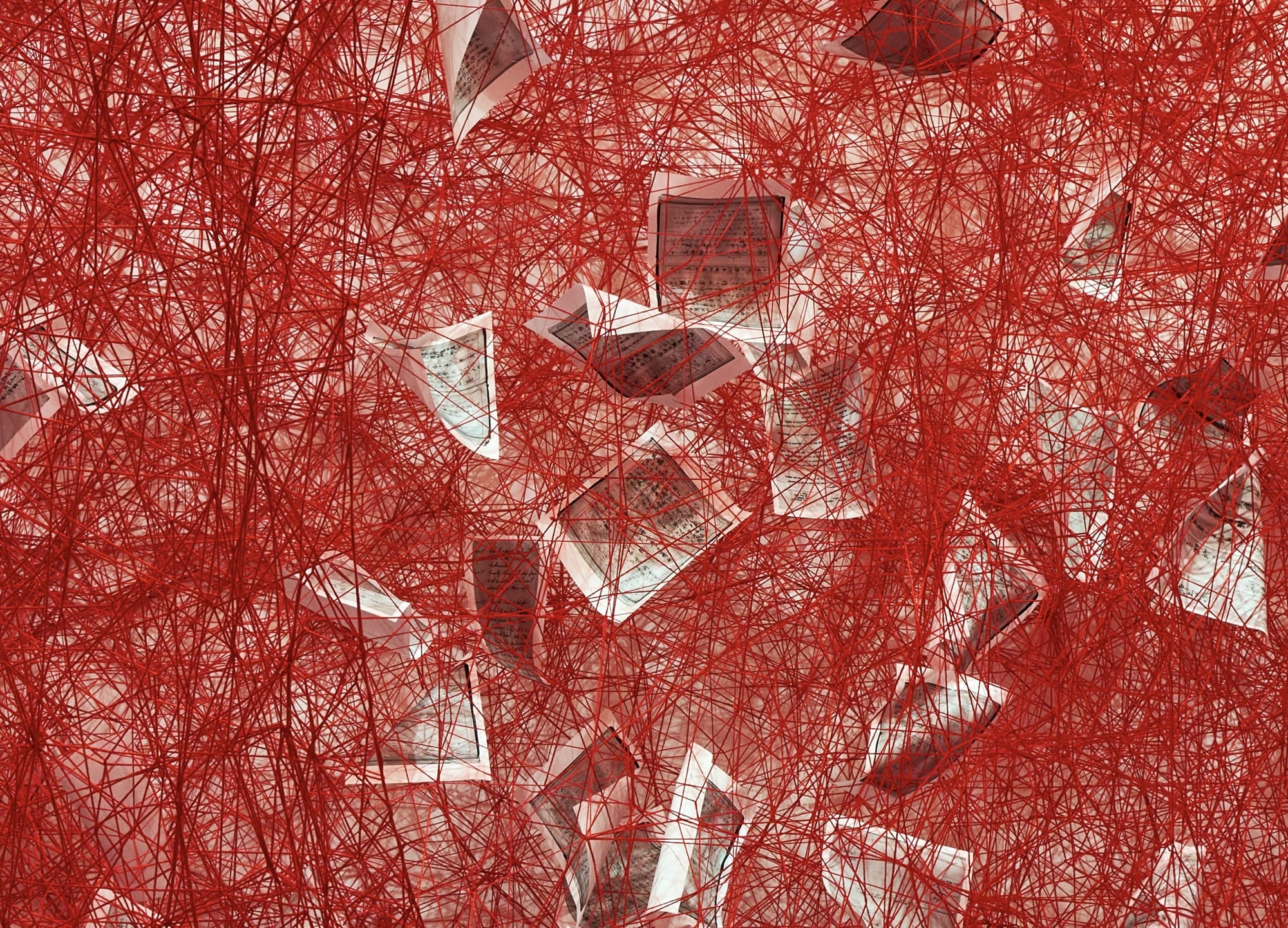a detail of a full-room installation of red fiber and paper pages by Chiharu Shiota